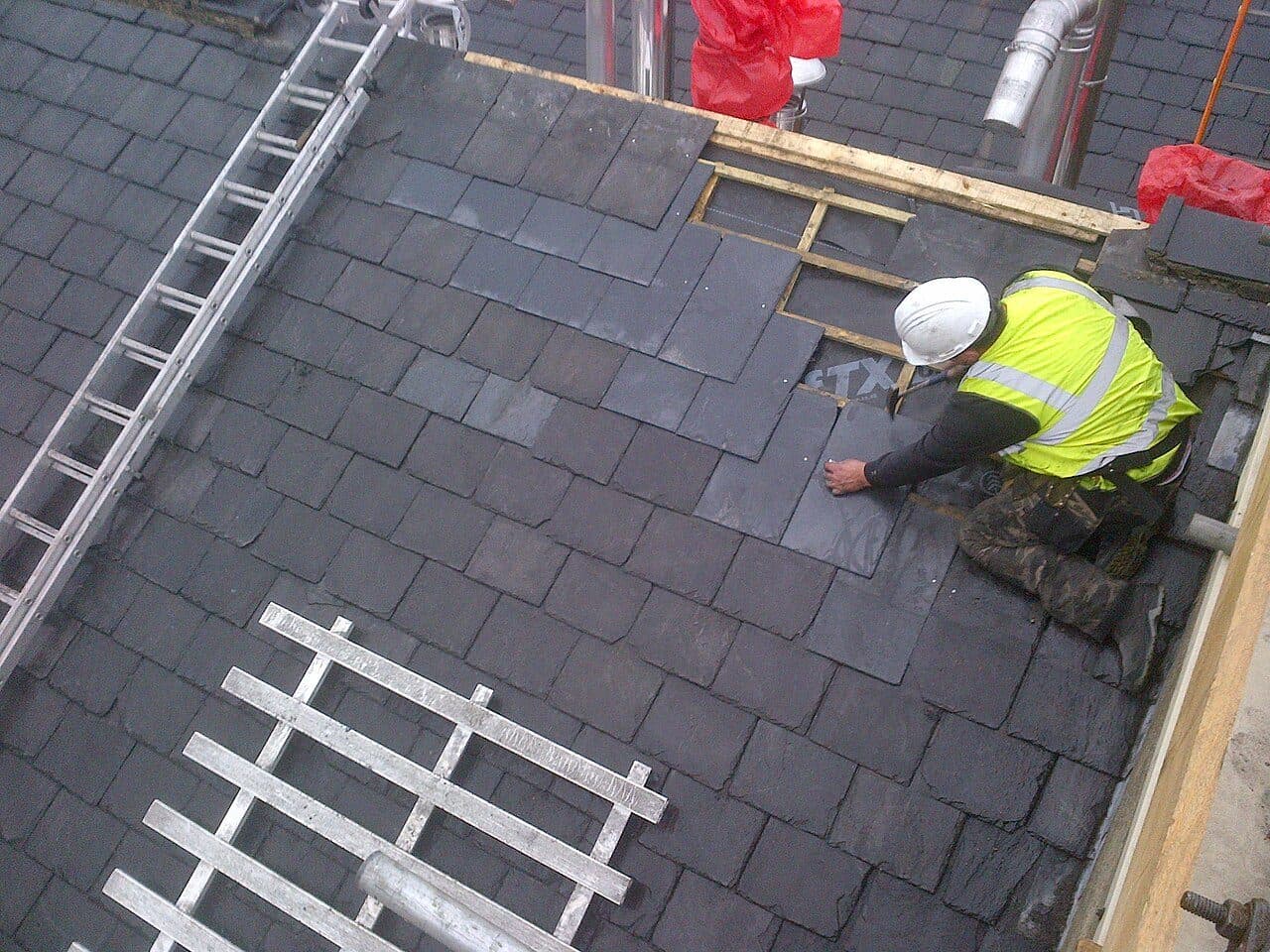Roofer in a white hard hat and hi-vis vest laying slate tiles