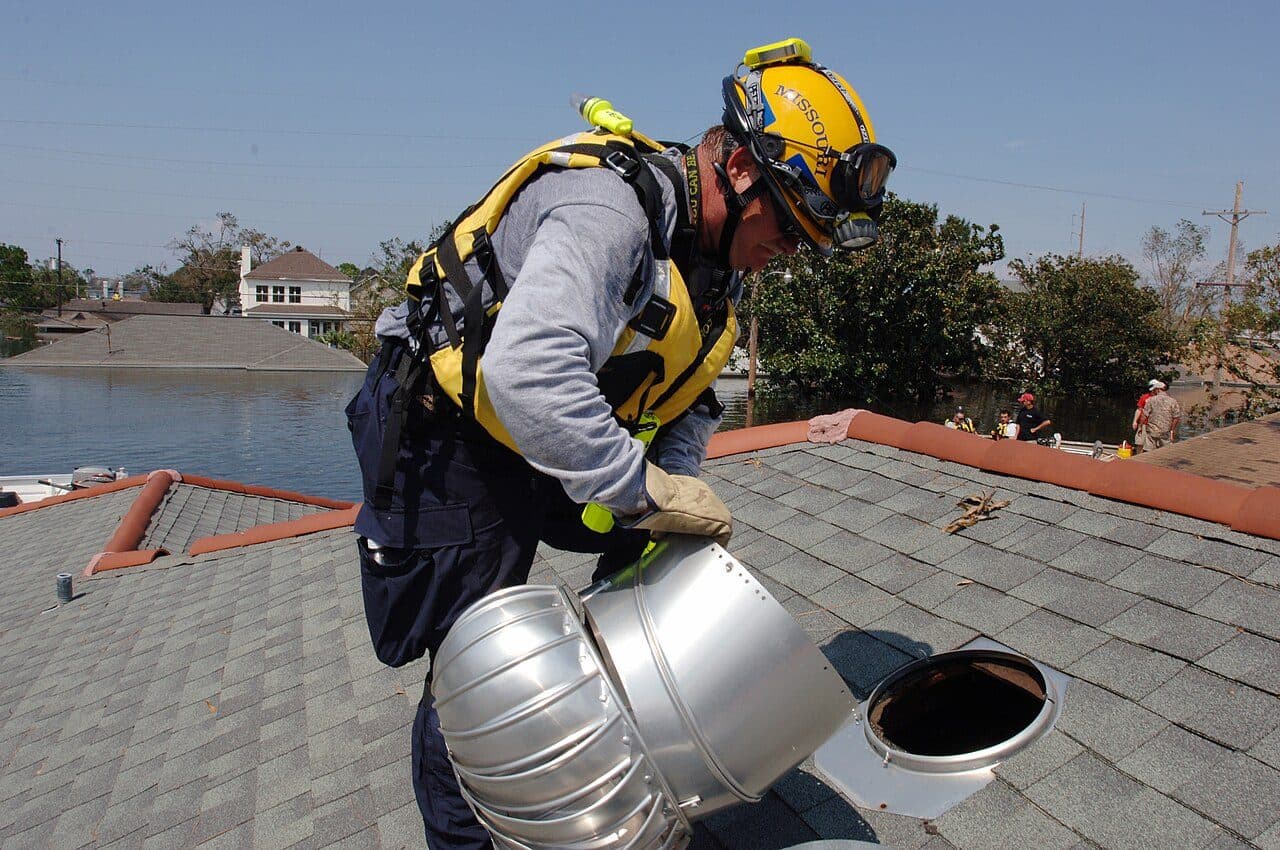 Roofer in a yellow helmet and harness working on a storm-damaged roof