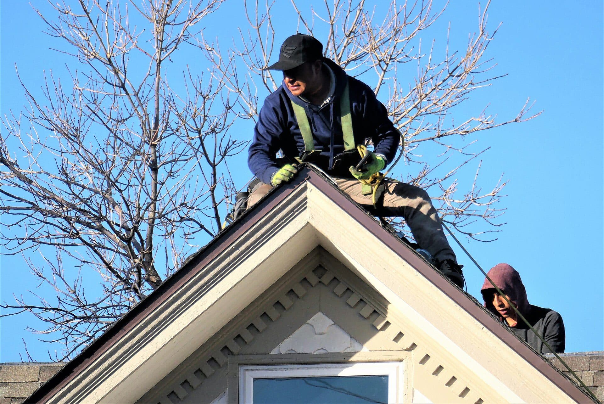 Roofer in a safety harness working along the ridge of a gabled roof