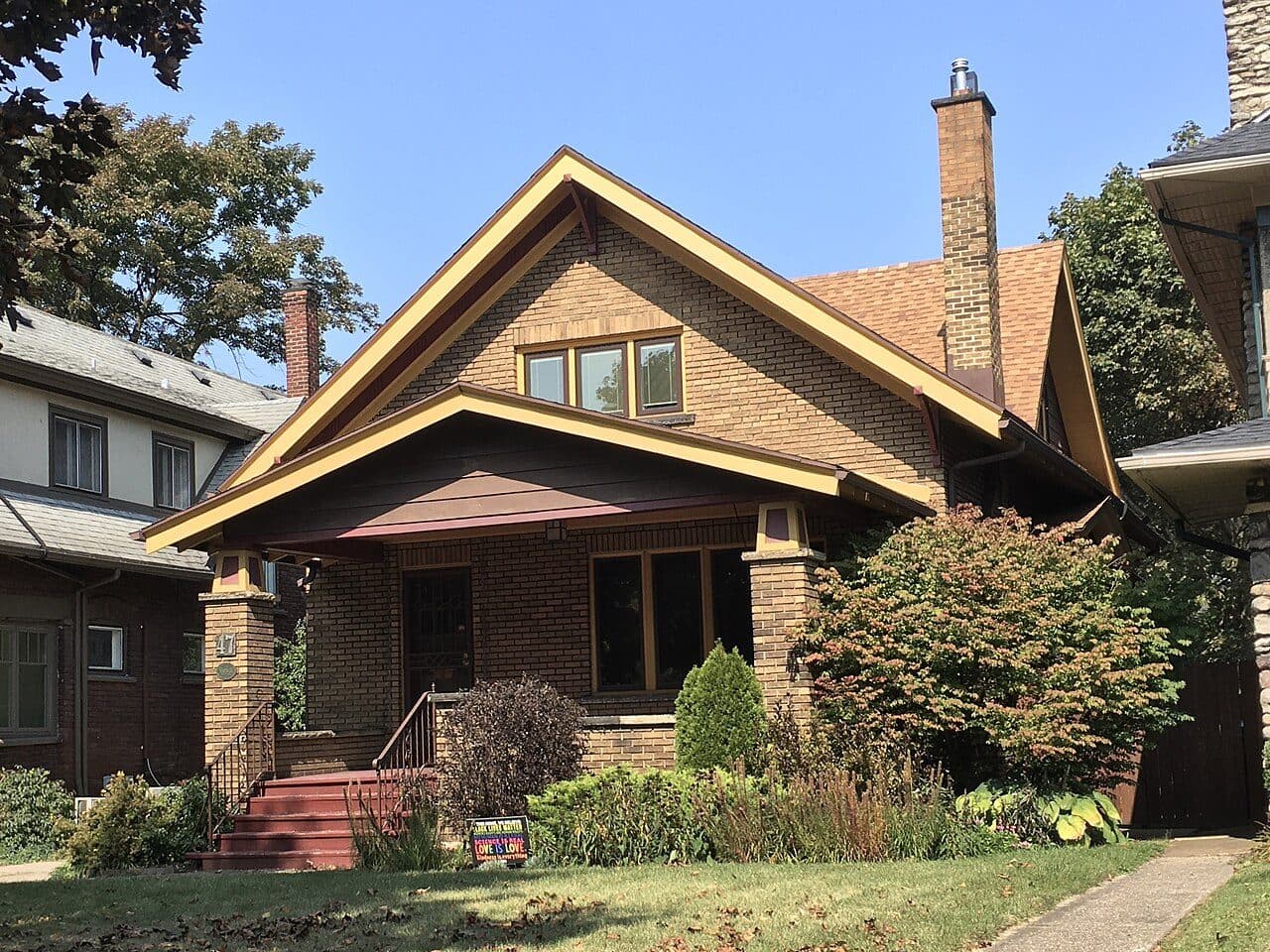 Craftsman bungalow with tan shingle siding, red trim and a brick chimney