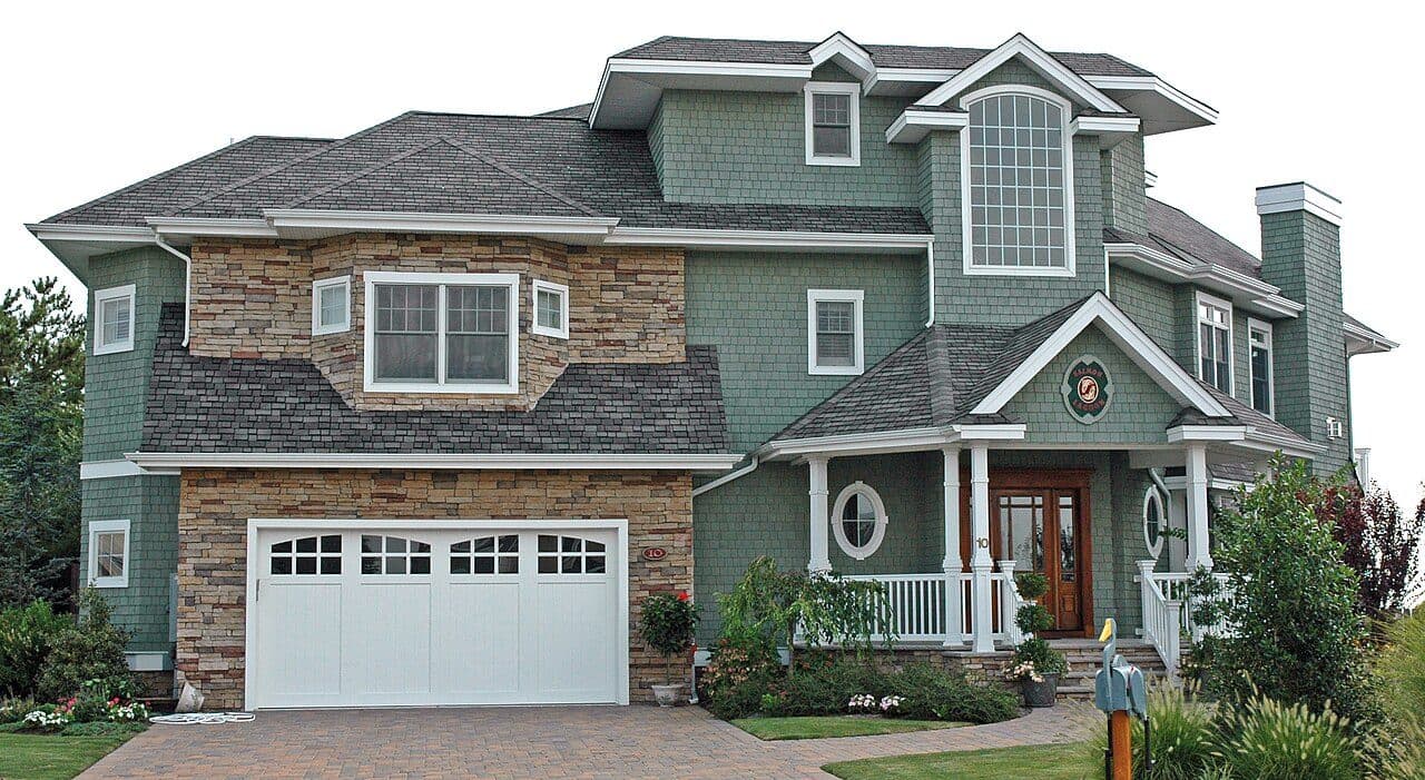 Green craftsman-style home with stone accents and a grey shingle roof