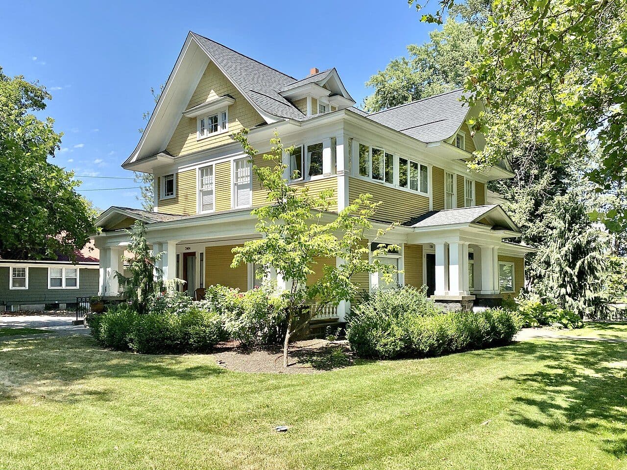 Yellow Victorian house with a grey shingle roof and wrap-around porch