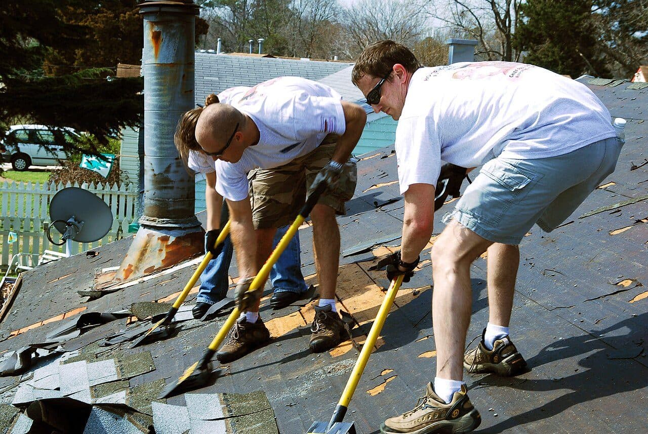 Two roofers scraping old roofing felt off a roof deck with shovels