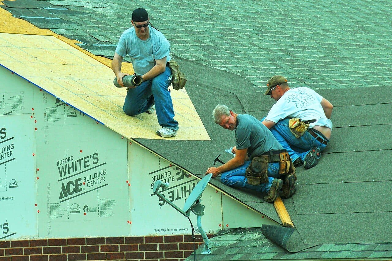 Three roofers rolling out underlayment over a new roof deck